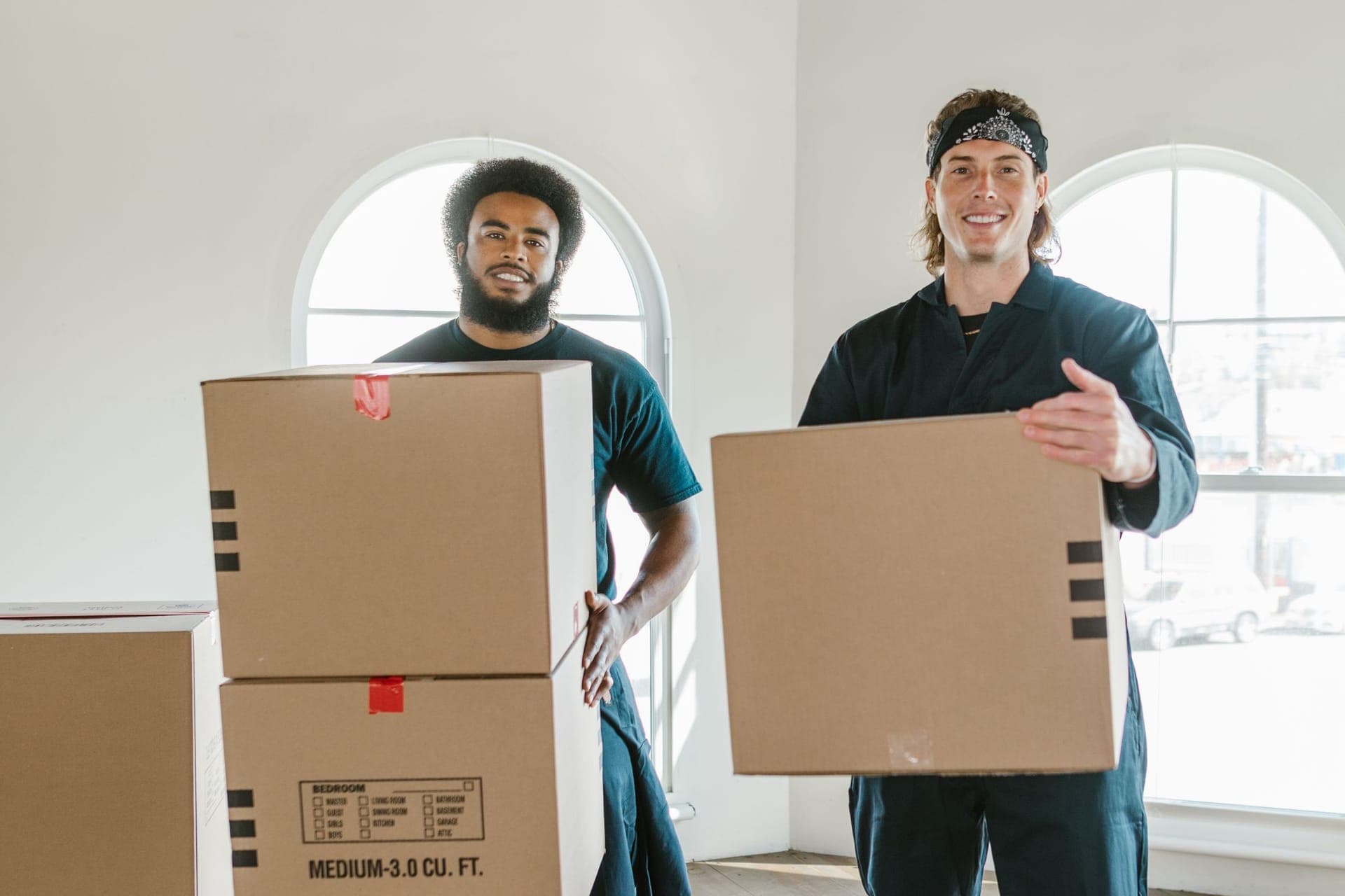 Zwei Umzugshelfer tragen Umzugskartons durch eine helle Wohnung