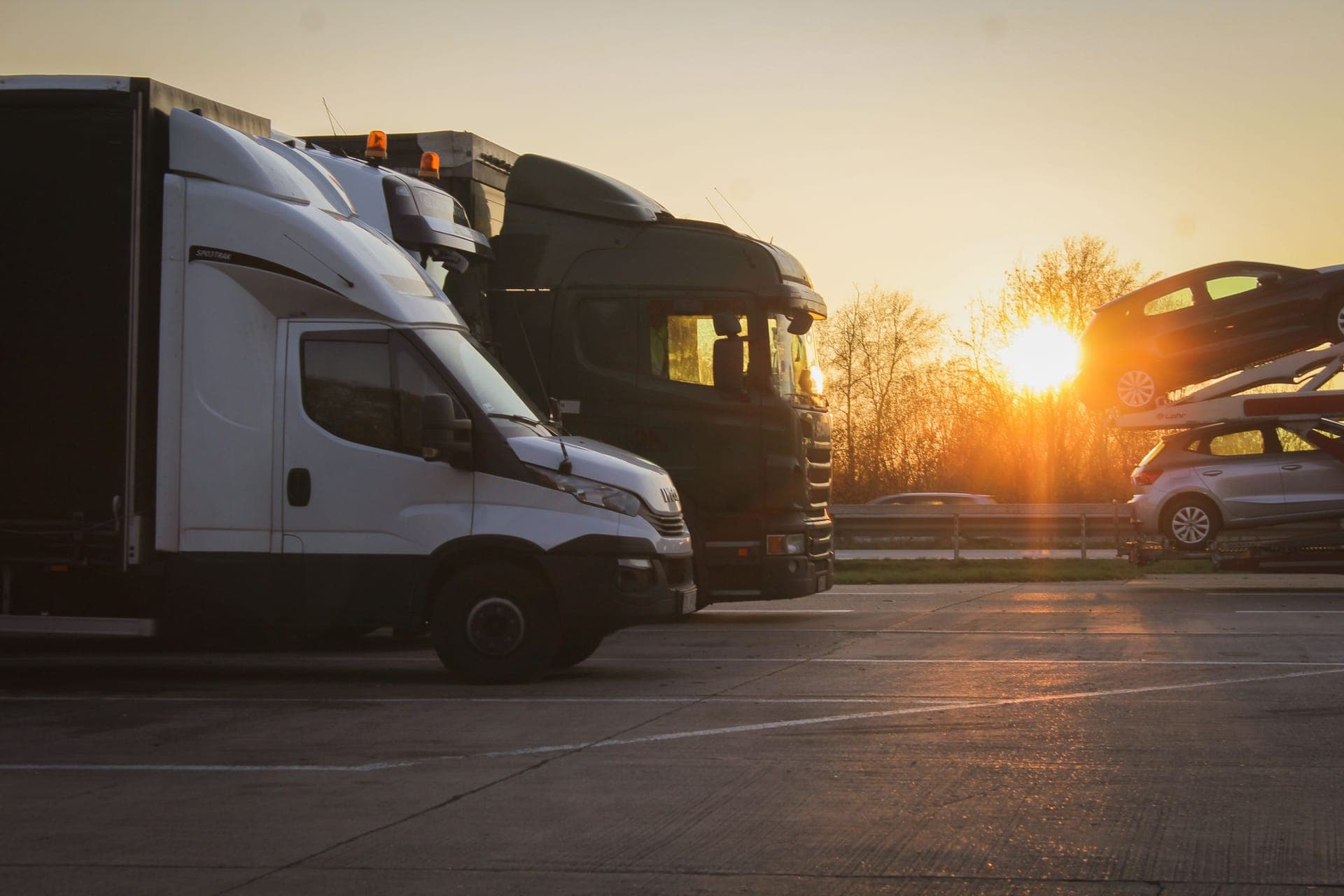 Van, lorry and articulated truck with a car transporter at a rest area at sunset